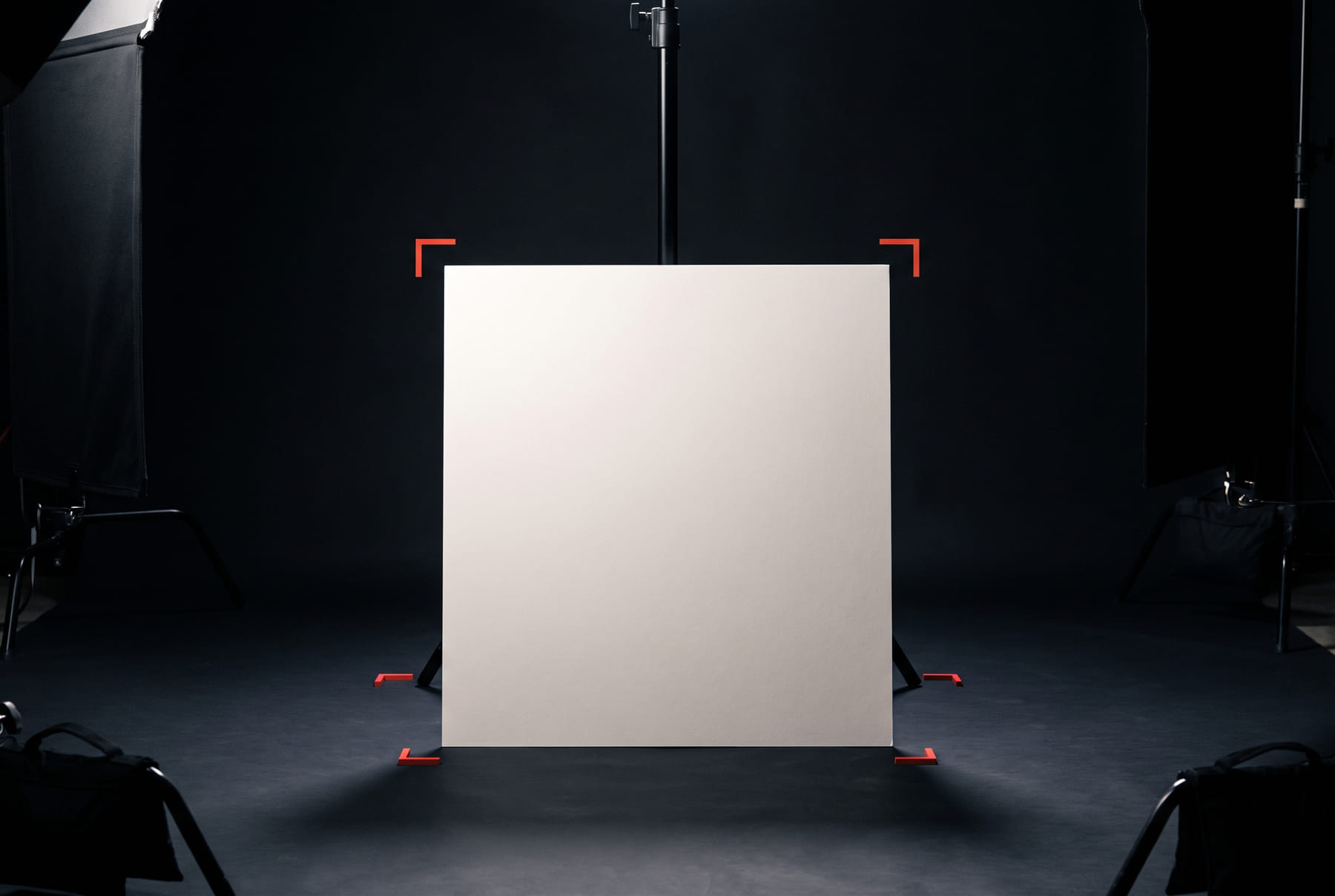 FIG.03 — a studio set lighting a completely blank matte panel on a stand, framed by four red crop marks, with grip equipment in silhouette at the edges