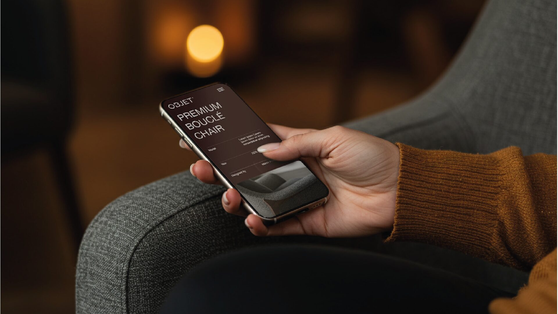 FIG.05 — the Objet product page held on a phone over the arm of a grey bouclé chair in warm lamplight